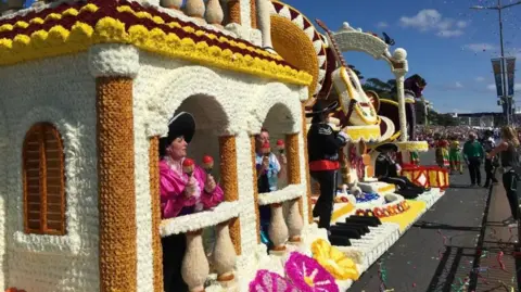 BBC People holding maracas on board a Mexican-themed floral float for Jersey's Battle of the Flowers parade