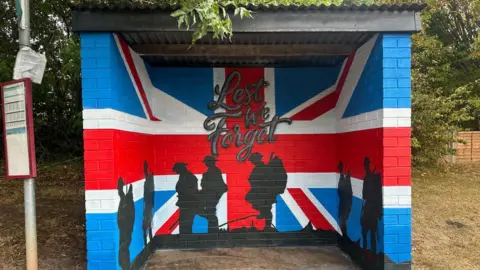 A bus stop painted with a design which includes silhouettes of soldiers and poppies on a union jack background