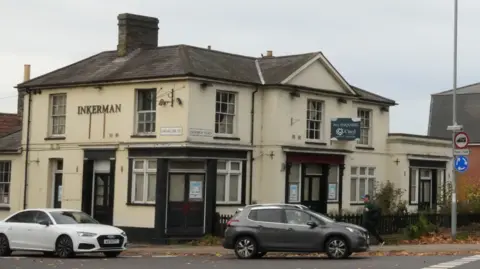 John Fairhall/BBC The Inkerman pub building taken from the opposite side of the road. The cream building is closed up with little sign of life. Several cars drive in front of it as they wait to enter a mini roundabout. 