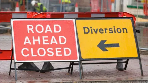 Two road signs, one saying 'road ahead closed' the other 'diversion' with an arrow underneath. The first sign is red and white and the second sign is yellow and black.