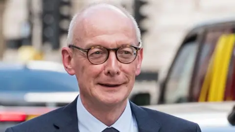 Getty Images Pat McFadden wearing round glasses and smiling while walking in Westminster