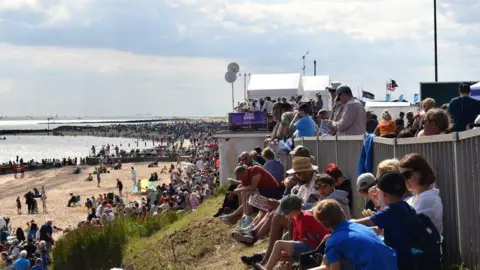 Tendring District Council Crowds watching the Clacton Airshow from the beach and standing area on above the sea barrier. 