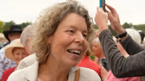 Connor Bennett/BBC Agnes Watson with dark blonde hair is talking to a reporter who is off camera. Crowds of people are behind her, with one member of the public holding up their phone to take a picture. 