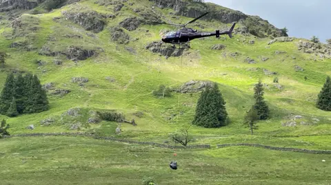 Helicopter carrying large bag of stones across Langdale Valley