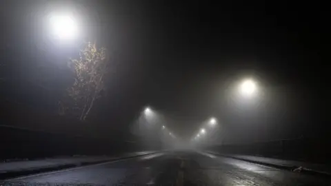 David Wall/ Getty Images Streetlights in the fog at night