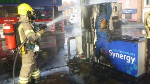 Tyne and Wear Fire and Rescue Service A firefighter hoses down a burnt petrol pump