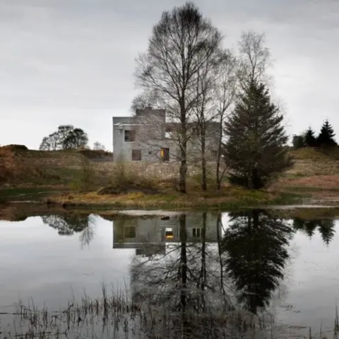 Gilbert McCarragher The grey, brutalist home stands close to a pond.