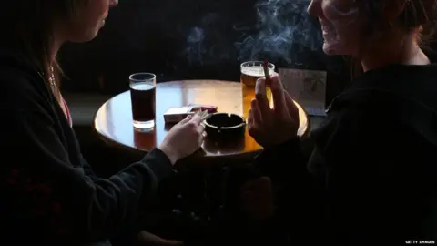 Getty Images Smoking bans were introduced across the UK between 2006 and 2007. People smoking in a pub.