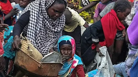 AFP A woman sitting on the ground surrounded by people in Nyala.
