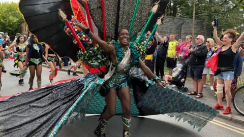 A woman parading down the street wearing an exotic costume with people cheering on the side of the road. 