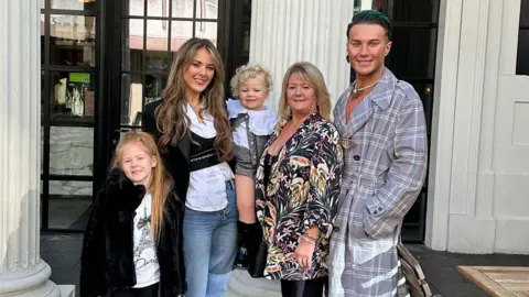 Handout James Lee Williams wearing a light grey trenchcoat, smiles for a picture with his mother, wearing a floral blouse, and sister, wearing a black coat over a white blouse. Her two young children are also smiling.