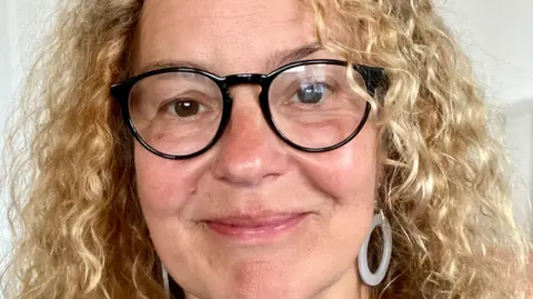 Literature Works Helen with curly blond hair and black rimmed glasses smiling at the camera.