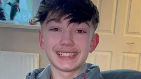 Christopher McBurnie, who has short brown hair with a long fringe and is wearing a grey jacket with a hood. He is smiling.