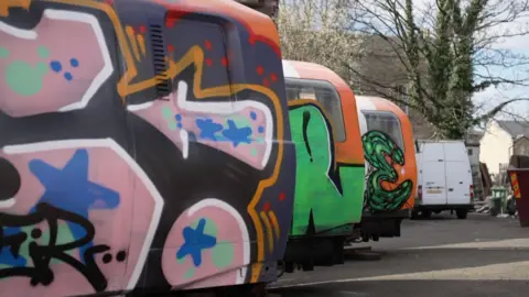 Three subway carriages in a row, they all have different coloured spray painted design on them.