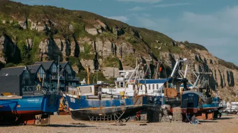 Fishing boats moored on the shingle beach at Hastings in the sunshine with cliffs behind