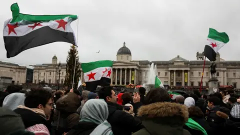 Reuters A crowd of people standing in London's Trafalgar Square, waving the flag of the Syrian opposition.