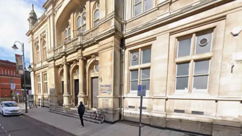 A large sandstone public building with columns and an ornamental balustrade over the entrance. 