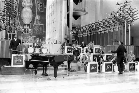 Getty Images Duke Ellington is seen standing conducting his orchestra in a black and white image with the modernist cathedral as a backdrop.