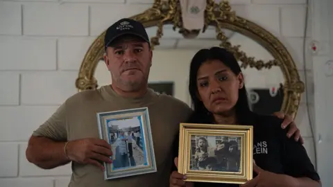 A man and a woman are seen holding photos of his dead son