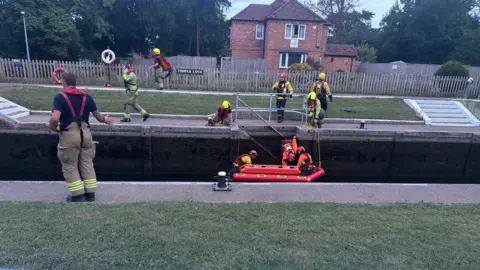 Wendy Hermon Firefighters lower a red boat into a river lock