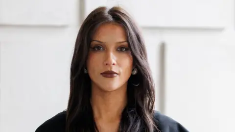 PA Media Cara Hunter has long dark hair and brown eyes. She is wearing a black top, silver earrings and dark brown lipstick.
