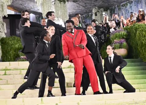 MG26/Getty Images para el Museo Metropolitano/Vogue. Joshua Henry actúa durante la Gala del Met 2026, dedicada al arte del vestuario, en el Museo Metropolitano de Arte el 4 de mayo de 2026 en Nueva York. Henry luce un esmoquin rojo cruzado con adornos plateados en las solapas. Se sitúa en las escaleras y canta mientras actúa para la prensa.