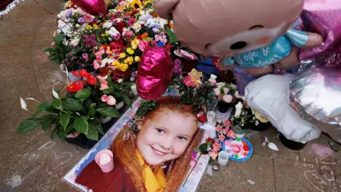 A picture of a little girl is on the ground surrounded by flowers and balloons- pink heart shapes and a teddy bear saying Love and Hugs