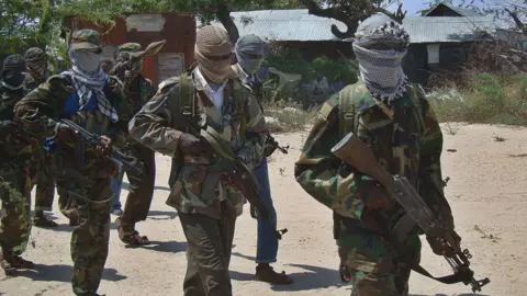 AFP Al-Shabab recruits in combat uniforms march while carrying guns. Their faces are covered with scarves.