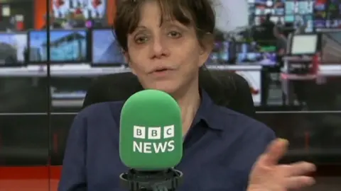 A women, Amy Heckerling, wears a navy shirt and talks into a green microphone