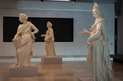 Wojtek Lubowiecki The three muses in the hall. Clio holds a book, Calliope holds two books, and Polyhymnia has a scroll.