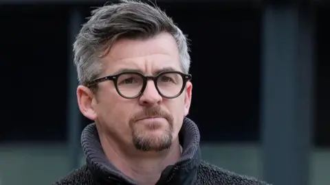 PA Media Joey Barton with grey hair and brown beard and black glasses wearing a grey jumper.