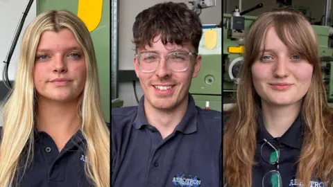 A composite image showing three people looking straight at the camera. Hope Hayden-Ferguson is on the left. She has long blonde hair, which is falling over her shoulders, and blue eyes. She is wearing a dark blue T-shirt. Myles Dillon is in the middle. He is smiling, showing his teeth, and is wearing clear plastic-framed glasses and a dark blue T-shirt. "Aerotron" is written on the chest of his T-shirt. On the right of the composite is Tegan Smith. She is smiling slightly and is wearing a dark blue top, with a pair of glasses folded and tucked into the collar. She has light brown coloured hair, which is falling over her shoulders. Large pieces of industrial machinery can be seen in the background of each image.