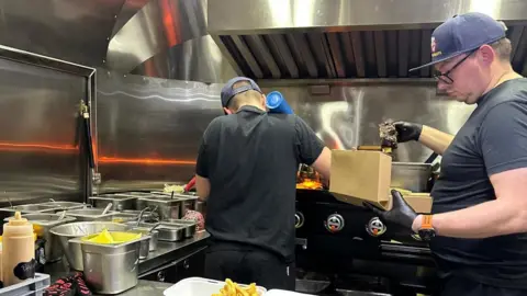 Karen Olejarka Greg Olejarka on the right and Dexter on the left and they are both cooking in the truck