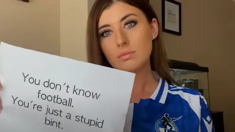 HerGameToo Woman with poster saying 'you don't know football. You're just a stupid bint'