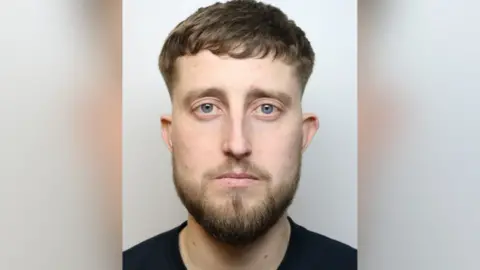 James Farmer's custody mugshot, he is seen wearing a black shirt. He has a beard and short hair.