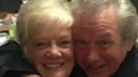 Sheila Jackson, who has blonde hair and is 83 years old, is photographed hugging her partner Peter Greener, 77, who has swept-back grey hair.