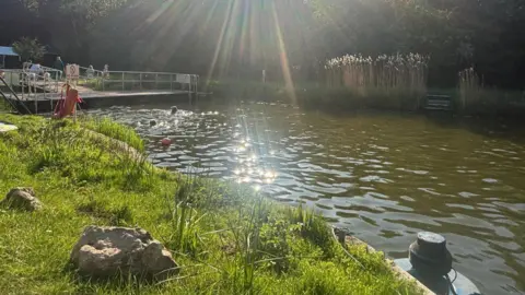 The sunshine glints on the water at Henleaze Lake in Bristol as swimmers paddle in the distance