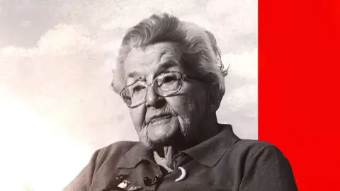 An elderly woman wearing glasses looks off camera