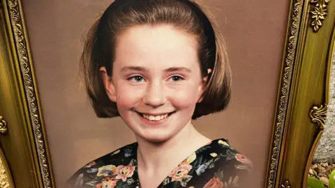 Fitzgerald family A photograph of a girl who is smiling. She has a short brown bob hairstyle and a flowery blouse on. The photo has a brown background and is in a gold frame. 