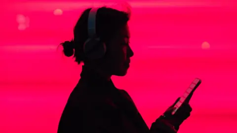 Woman in silhouette listening to music on smarphone in front of a bright pink background