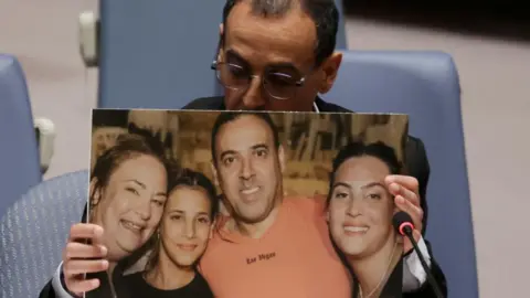 Reuters Eli Sharabi, his head downcast, holds an enlarged picture of himself with his wife and daughters.