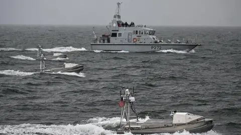 Getty Images Three small unmanned boats sail through choppy grey seas in front of a larger grey navy boat 