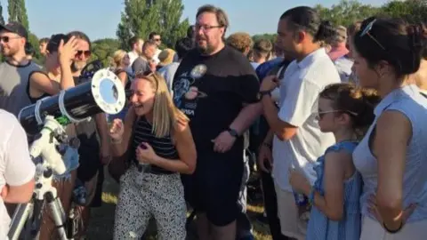 Jade Taylorson/BBC People view the eclipse via a telescope in Heaton Park in Manchester
