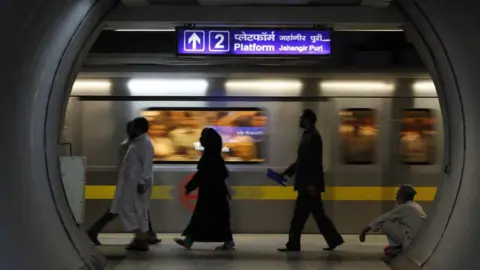 Universal Images Group via Getty Images The silhouette of men and women walking on a platform at Jahangir Puri metro station in Delhi. 