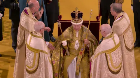 The King takes part in his coronation surrounded by clerics
