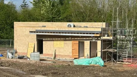 Friends of Bennerley Viaduct A half-built building in honey-coloured blocks with a flat roof, scaffolding to one end, and bare earth around it. 