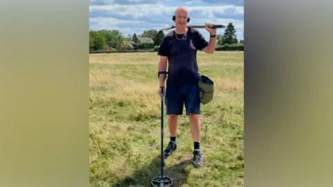 Man standing in a field with a metal detector