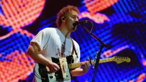 Sam Fender singing and playing a guitar on stage.