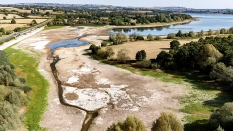An aerial image of an estuary with trees and fields and a very dry, brown river bed, with little water in it.