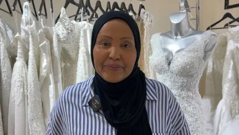 Leyla Ali in front of a row of wedding dresses